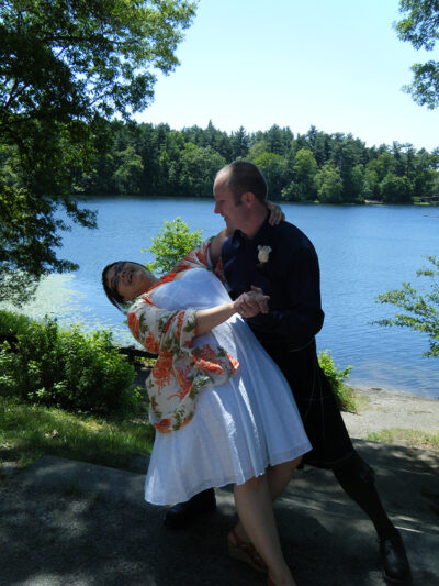 Gus dips wedding-dress-clad Andi in front of a tree-lined lake.
