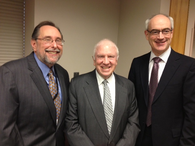 Three men pose together, smiling, in suits.