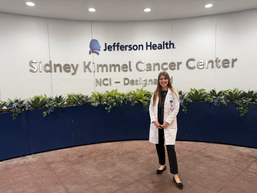 Yuliia Lozko, a radiation oncologist at NCI of Ukraine, standing in front of a sign that says Jefferson Health, Sidney Kimmel Cancer Center.