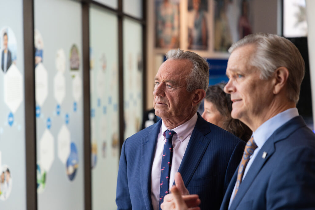 Stone appears to be showing Kennedy a City of Hope display and talking about it while Kennedy listens.