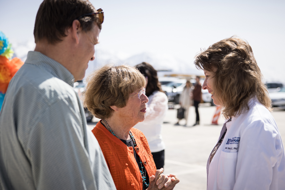 Dr. Ulrich speaks with Karen as Mark looks on at an outdoor event.
