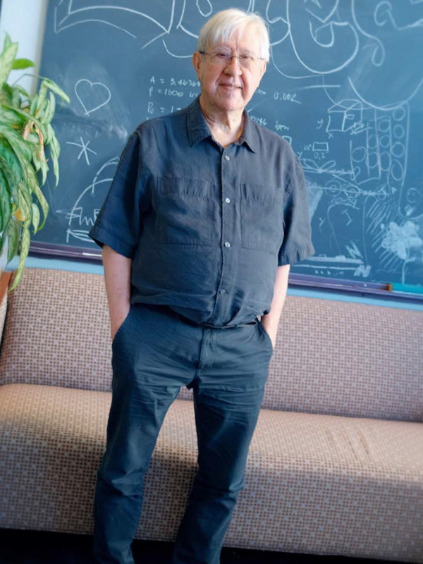 Dr. Szalay stands in front of a green chalkboard with chalk sketches and scribbles.