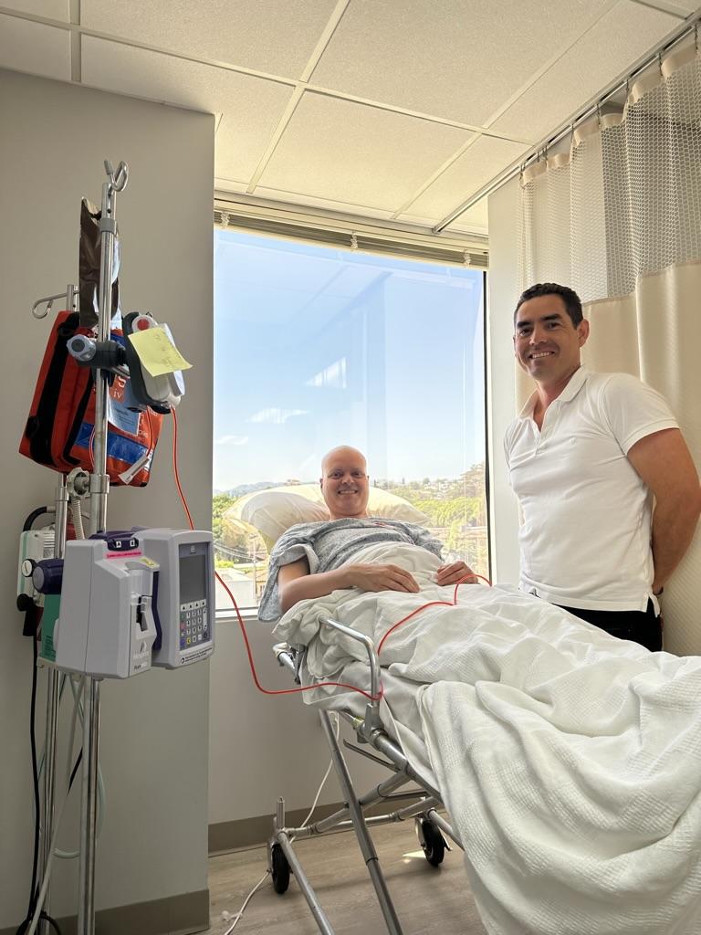 Sijbrandij lays in a hospital bed as Mej&iacute;a Oneto smiles nearby.
