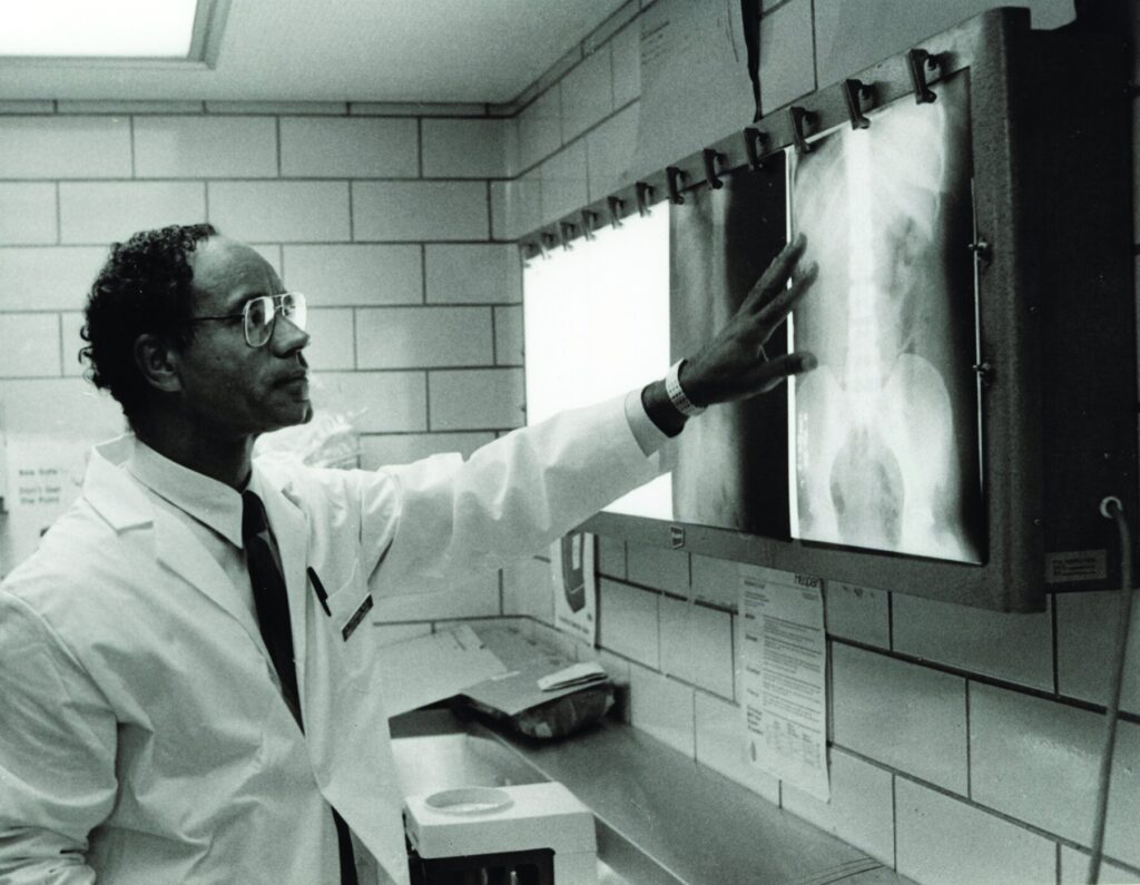 Freeman in a white coat with his hand pointing to a back-lit abdominal x-ray.