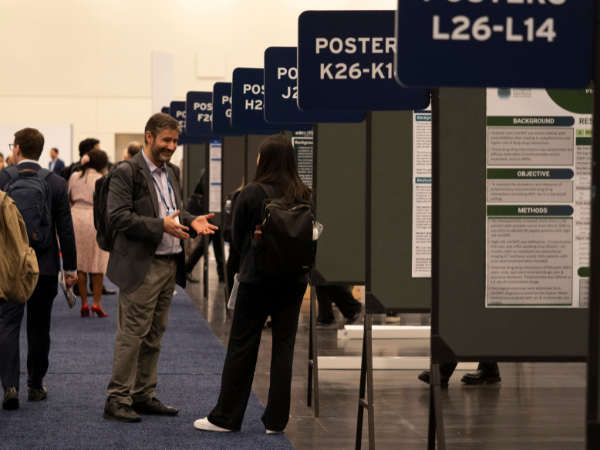 Conference goers milling about a poster session, engaged in conversation.