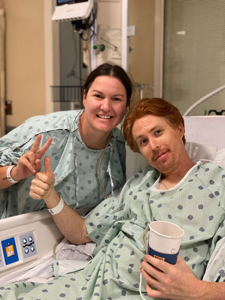Herzer in a hospital bed with his cousin standing next to him, both wearing hospital gowns.